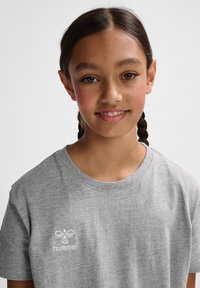 Grå kortærmet t-shirt lavet af blødt stof med rund halsudskæring, prydet med et hvidt broderet logo på venstre brystområde.