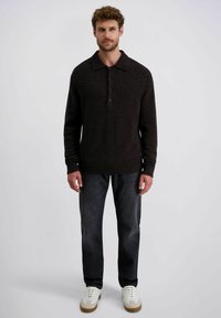 Dunkelbrauner Pullover mit Kragen, Knopfleiste, gerippten Bündchen und Saum. Getragen mit dunklen Jeans und weißen Sneakers. Glatte Textur.