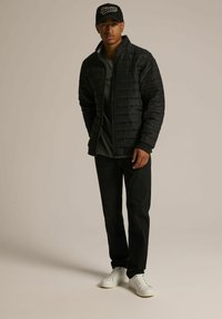 Czarna kurtka puchowa z poziomym pikowaniem, zaokrąglony kołnierz, zestawiona z ciemnymi dżinsami i białymi trampkami. Model nosi czapkę w kolorze czarnym.