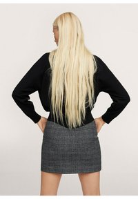 Maglione nero con vestibilità ampia e maniche lunghe abbinato a una mini gonna grigia a quadri, con un motivo testurizzato. Capelli biondi lunghi e lisci.