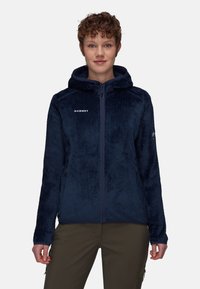 Marinblå fleecejacka med ett strukturerat mönster, dragkedja och huva. Har en logotyp på bröstet och sidofickor. Mjuk material.