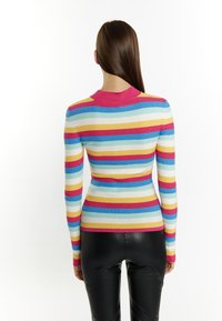 Maglione a righe multicolori con texture a coste, colletto rotondo rosa e silhouette aderente contornata. Indossato con pantaloni neri.