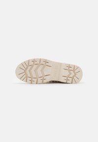 Suola di una scarpa realizzata in un materiale di gomma beige chiaro, texture antiscivolo, con un motivo a zigzag e un marchio impresso al centro.