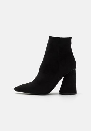 Schwarze Knöchelstiefel aus weichem Wildleder, mit spitzem Zehenbereich und einem massiven, geometrischen Absatz. Glatte Textur ohne sichtbare Verzierungen.