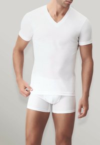 T-shirt bianco a V e boxer bianchi, entrambi con maniche corte e una texture morbida ed elastica, presentati su uno sfondo neutro.