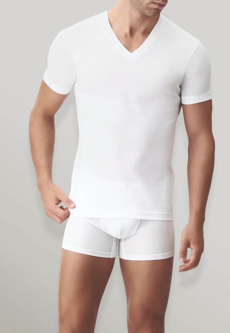T-shirt bianco a V e boxer bianchi, entrambi con maniche corte e una texture morbida ed elastica, presentati su uno sfondo neutro.