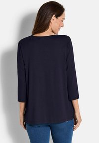 Navyblaue Bluse mit Dreiviertelärmel, lockerer Passform, glattem Material und rundem Ausschnitt, kombiniert mit hellblauen Jeans.