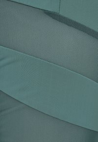 Tessuto testurizzato con motivi variabili in tonalità di turchese, caratterizzato da sezioni morbide e in rete. Notevole gradiente di colore e elementi di design a strati.