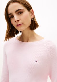 Ριμπ πουλόβερ σε ανοιχτό ροζ χρώμα με λαιμόκοψη βάρκα, διαθέτει μικρό κεντημένο λογότυπο στην αριστερή πλευρά του στήθους. Μαλακή υφή και εφαρμοστό σχέδιο.