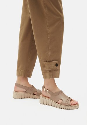 Bež kožne sandale s otvorenim prstima, podesivim remenom i teksturiranim potplatom. U kombinaciji s smeškim hlačama.