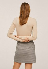 Langarm-beige Oberteil mit gerafften Manschetten, kombiniert mit einem taillierten karierten Minirock, der ein klassisches Muster in Schwarz und Weiß zeigt.