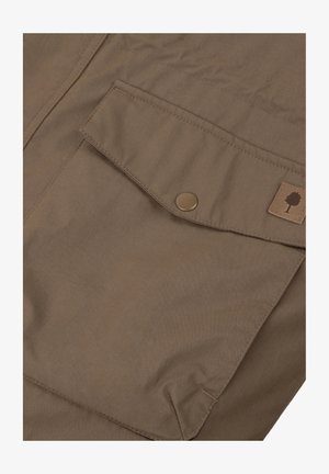 Tessuto marrone dalla superficie liscia, con una tasca a pattina chiusa da un bottone rotondo e un piccolo logo ad albero su una toppa beige.