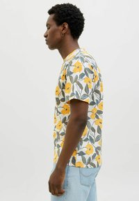 Tricou cu mânecă scurtă, alb, cu un model floral ce include flori galbene și frunze verzi; croi lejer, gât rotund, material moale.