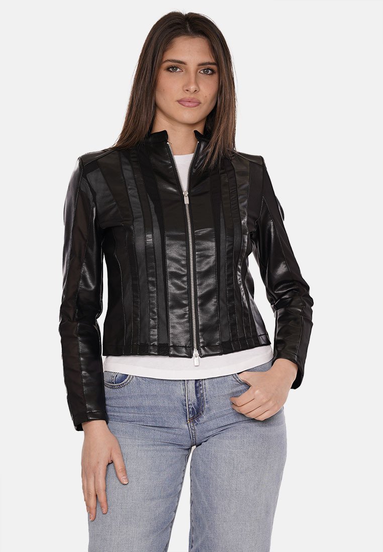 Giacca in finta pelle nera con design a righe verticali, chiusura con zip, taglio corto e colletto rialzato, abbinata a una maglietta bianca e jeans blu.