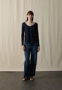 Navy long-sleeve shirt with a wide V-neck, paired with blue wide-leg jeans and brown sandals, set against a neutral background.