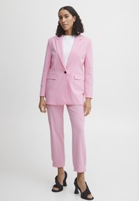 Pink blazer and matching pants in a structured design, made of smooth fabric. Black heels complete the outfit. Texture appears soft and sleek.