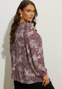 Camicia a maniche lunghe di colore bordeaux con motivo floreale bianco, caratterizzata da maniche arricciate e una vestibilità comoda, realizzata in tessuto morbido e leggero.