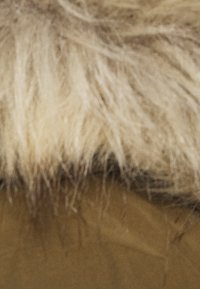 Faux fur trim in light beige atop a khaki fabric, featuring a soft, fluffy texture and a seamless integration with the garment.