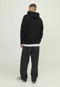 Zwarte hoodie met een kangoeroezak, gecombineerd met loszittende donkergrijze jeans en sneakers. De stof lijkt zacht met een klassiek design.