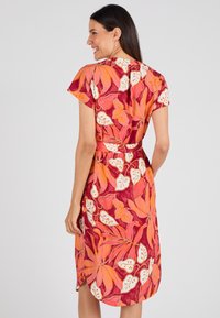Robe à manches courtes en tissu léger, arborant un motif floral vibratoire en rouge, orange et blanc, avec une taille cintrée et des fentes sur les côtés.