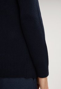 Navyblauer gestrickter Pullover mit einem gerippten Muster, engen Ärmeln und geradem Saum, mit einer glatten Oberfläche und ohne sichtbare Hardware oder Akzente.