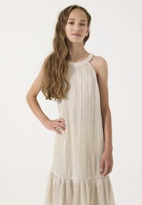 Vestido plisado sin mangas en beige claro con un dobladillo rizado. Hecho de una tela suave con un brillo sutil, presenta un escote redondo.