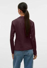 Burgundský blazer s přizpůsobeným střihem, zapínáním na jeden knoflík a dvěma bočními kapsami, spárovaný se světle modrými vysokými džíny.