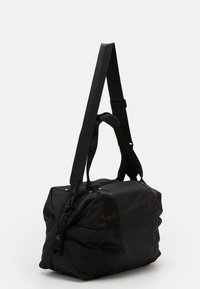 Sac de voyage noir en tissu durable, doté d'une bandoulière rembourrée, de poignées supérieures et de panneaux contrastés pour un aspect texturé supplémentaire.