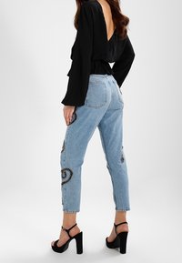 High-waisted light blue jeans with black embroidered snake patterns, paired with black strappy heels and a black long-sleeve top.