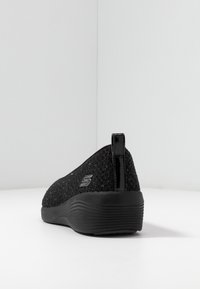 Černá nazouvací bota s texturovaným pleteným svrškem, lesklým zadním dílem a gumovou podrážkou. Obsahuje logo na boční straně.