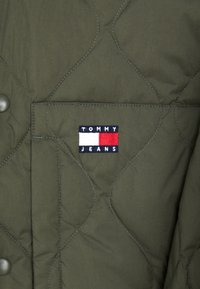 Groene gewatteerde jas met een drukknoopsluiting en een borstzak. Inclusief een geborduurd 'TOMMY JEANS' logo in blauw, wit en rood.