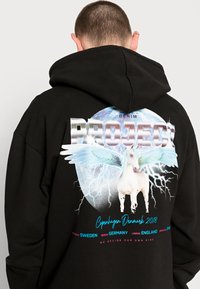 Felpa nera con cappuccio caratterizzata da una grafica colorata sul retro che presenta un unicorno, fulmini e il testo "PROJECT DENIM COPENHAGEN DANIMARCA 2018."