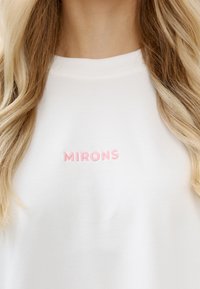 Witte sweatshirt met een ronde hals heeft roze geborduurde tekst "MIRONS" op de borst. Zachte stof en een relaxte pasvorm zijn duidelijk zichtbaar.