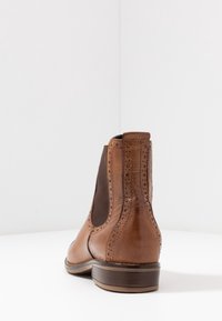 Ruske nahkatossut nilkkojen ympärillä elastisilla sivupaneeleilla, brogue yksityiskohdilla, pyöreällä varvalla ja matalalla pinnoitetulla korolla. Pehmeä rakenne ja kiiltävä viimeistely.