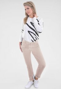 Witte trui met zwarte abstracte strepen, beige comfortabele sweatpants en witte sneakers. Casual outfit met een trekkoord in de taille en zijzakken.