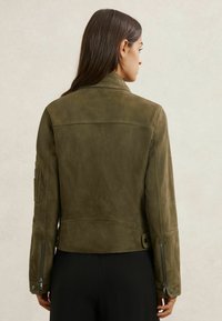 Õlivärvi rohelise seemisnahast jakk kraega, keha järgiva lõike ja tõmblukkudega varrukate äärtega. Detailidena on õmblused ja nööpidega taljekohandamine.