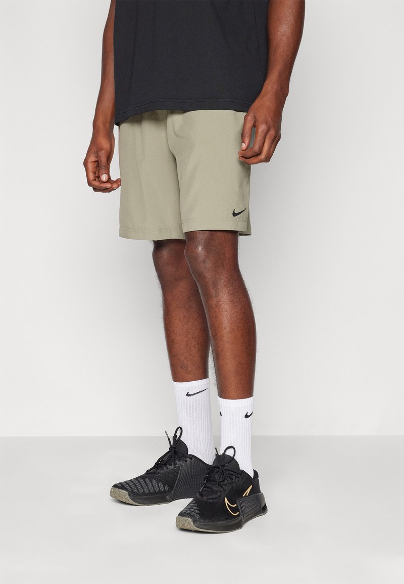 Khaki Nike-shorts hebben een relaxte pasvorm, een gladde stof en een zwart logo. Gecombineerd met zwarte sportschoenen en witte sokken met een logo.