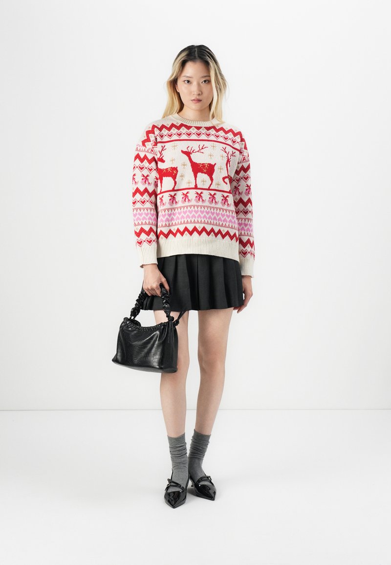 Suéter de punto rojo y crema con renos y copos de nieve, falda negra plisada, calcetas grises, bolso negro con textura y zapatos de punta.