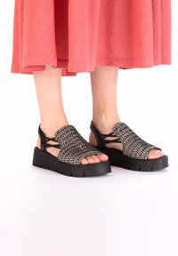 Sandales tissées noir et blanc avec une semelle épaisse noire. orteils ouverts et design à brides croisées pour le soutien du pied. Matériau supérieur texturé.