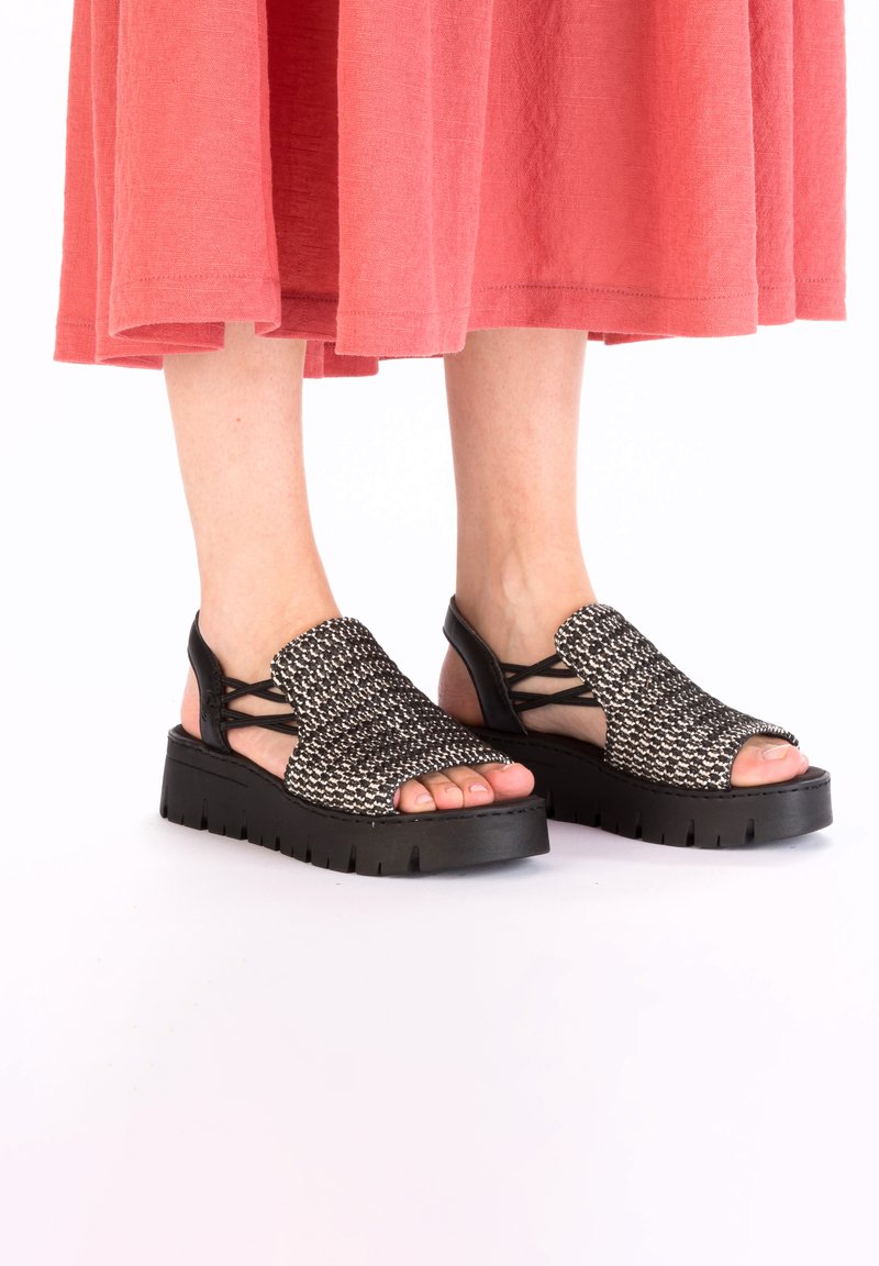 Sandales tissées noir et blanc avec une semelle épaisse noire. orteils ouverts et design à brides croisées pour le soutien du pied. Matériau supérieur texturé.