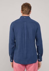 Marineblauwe blouse met lange mouwen van lichtgewicht stof, met een knoopsluiting bij de kraag en manchetten, en een rugplooitje voor extra comfort.