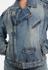 Close-up van een denimjack met een rits aan de voorkant en zijzakken, met een licht versleten, vervaagde blauwe textuur.