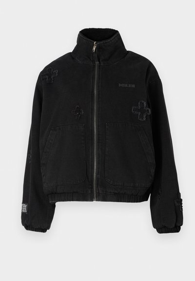 Black jacket made of cotton with a zip front, featuring two front pockets, embossed logo, and textured cross designs on the fabric.