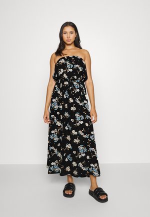 Black floral maxi dress with a strapless design, featuring blue and white flower patterns, cinched waist, and draped fabric. Worn with black slides.