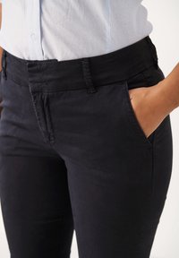 Zwarte katoenbroek met een zachte textuur, slim fit en zijzakken, met een verborgen tailleband en subtiele stikseldetails.