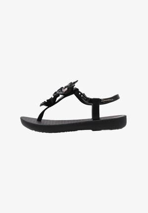 Sandalias de goma negras con un acento floral, que presentan una suela plana y una correa ajustable. Plantilla texturada para mayor comodidad. Diseño ligero.