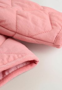 Giacca trapuntata rosa con polsini a costine, realizzata in un tessuto liscio e resistente, con motivo a rombi sulle maniche.