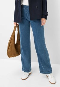 Bredde jeans i mid blå vask, med en subtil falmet tekstur. Kombineret med hvide sneakers og en brun ruskinds tote taske.