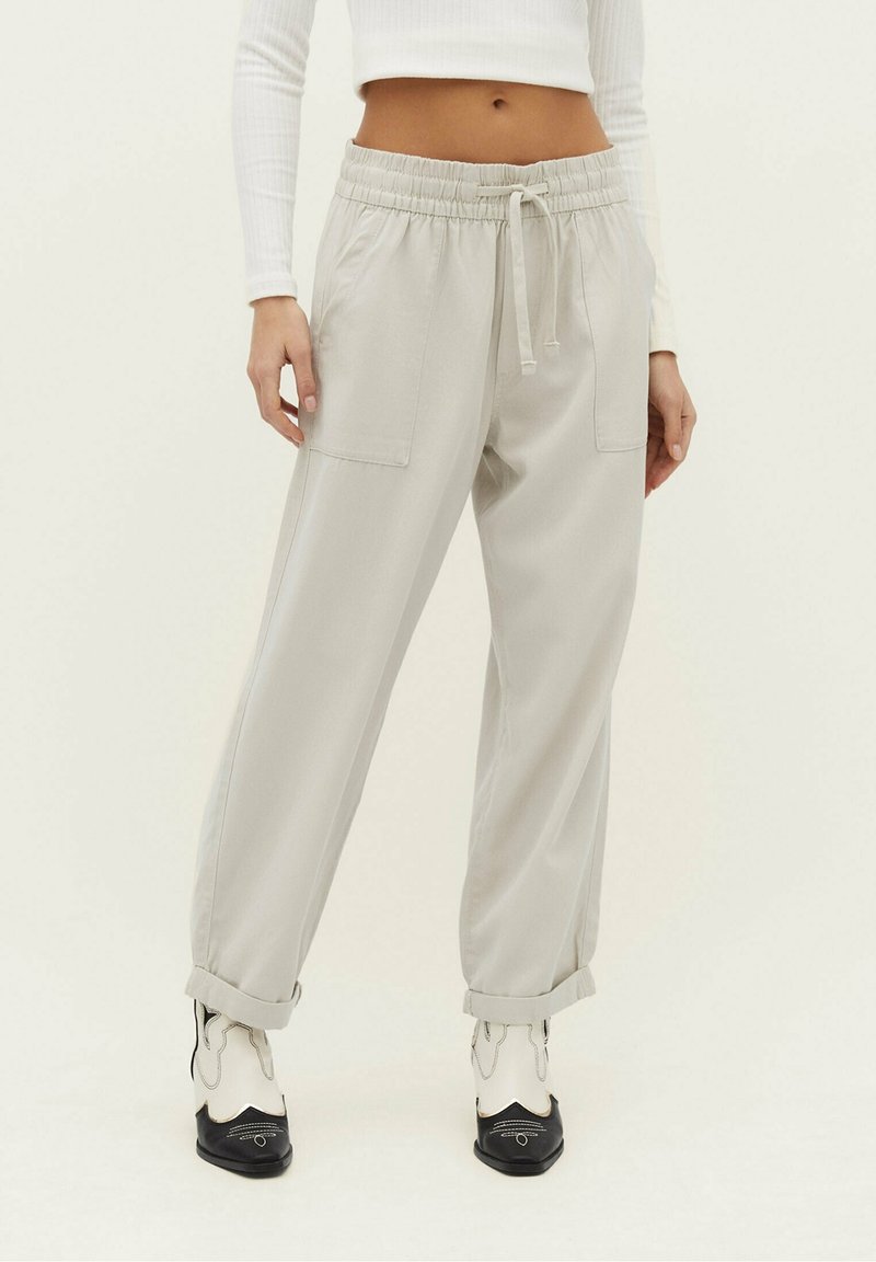 Femme portant un pantalon beige clair à cordon avec des revers roulés et des bottes western blanches et noires.