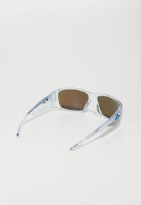 Klare Plastiksonnenbrille mit braunen Gläsern, aerodynamischer Form und strukturierten Bügeln, die ein blaues Akzentlogo und rote Hardware-Details aufweisen.